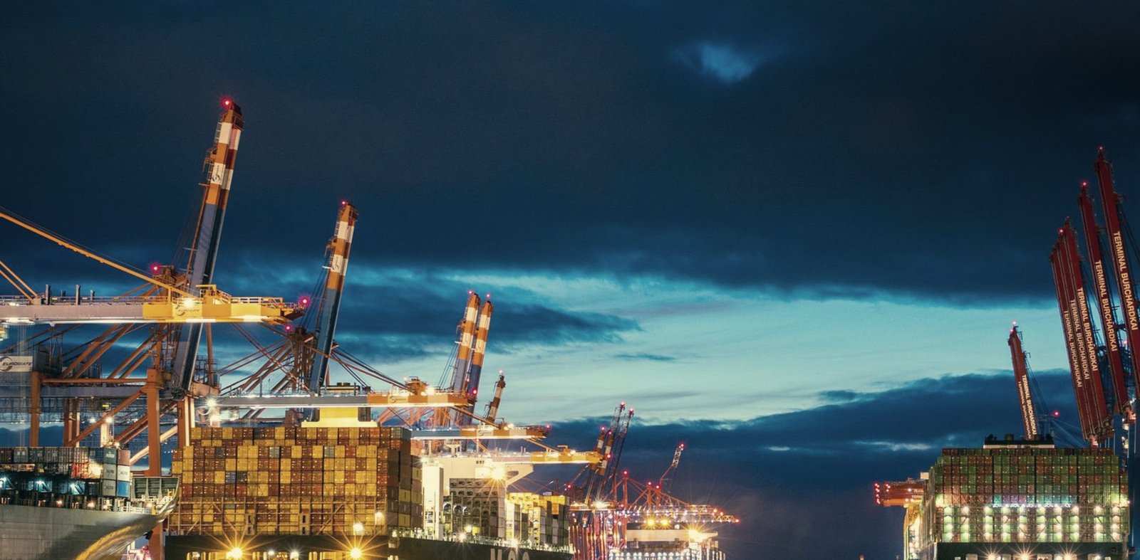 A lit container terminal at blue hour, gantry cranes over the quay