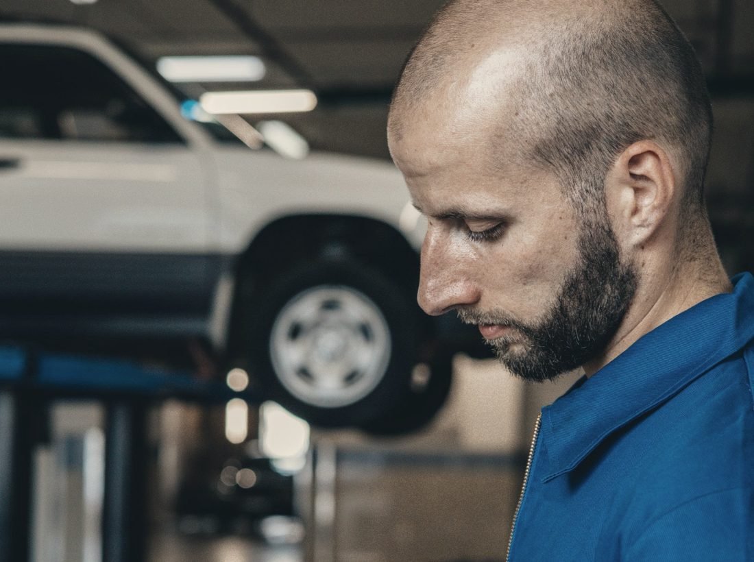 A mechanic in the workshop, a vehicle on the lift behind him