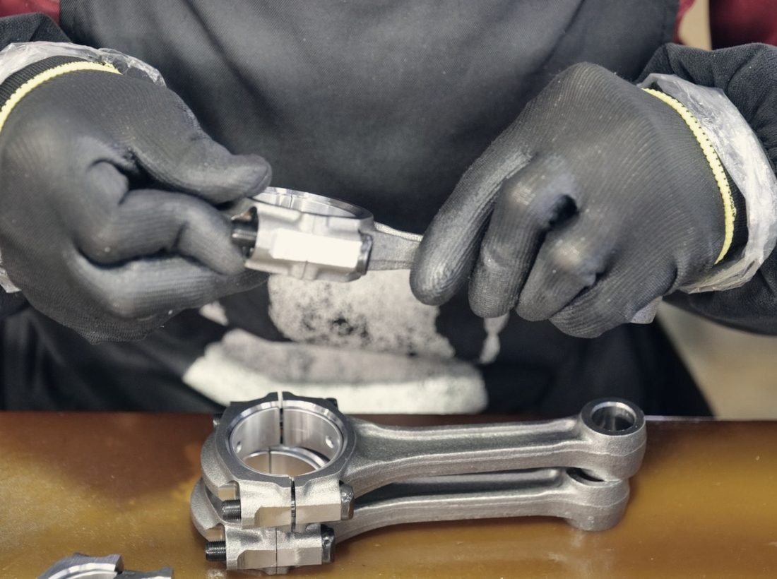 Gloved hands measuring a connecting rod on the bench